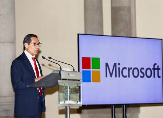 Mexico Finance Minister Rogelio Ramirez de la O standing at a podium beside a large monitor that bears the name and logo of Microsoft