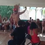 Video capture image of male strippers entertaining women who surround them in chairs.