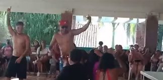 Video capture image of male strippers entertaining women who surround them in chairs.