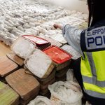 Police officer pointing at hundreds of methamphetamine parcels in clear plastic wrap confiscated in a Sinaloa Cartel meth bust in Spain