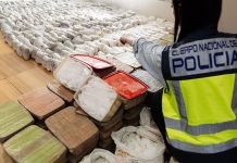Police officer pointing at hundreds of methamphetamine parcels in clear plastic wrap confiscated in a Sinaloa Cartel meth bust in Spain