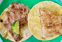 Two tortillas with meat on top, presented on a green plate and with a lime wedge