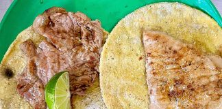 Two tortillas with meat on top, presented on a green plate and with a lime wedge