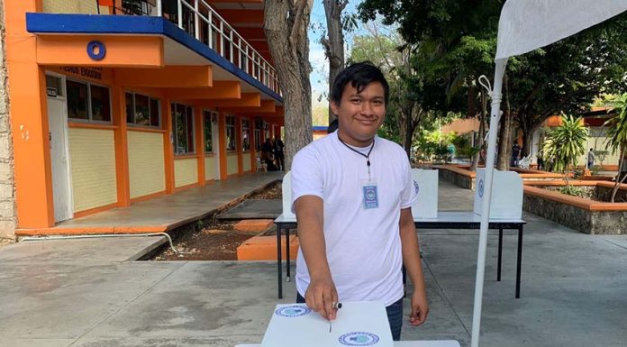 Smiling Mexican college student in a tee shirt and jeans placing a ballot in a box for a mock presidential election