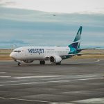 WestJet plane on a runway with a worker guiding the plane from outside