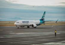 WestJet plane on a runway with a worker guiding the plane from outside