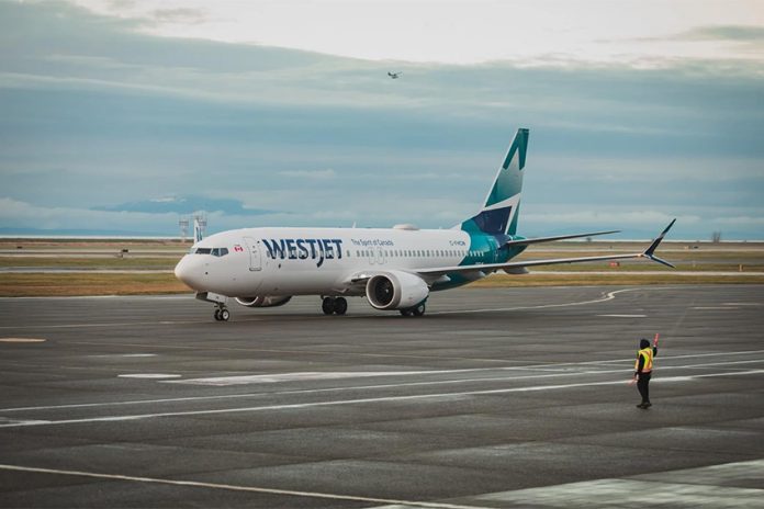 WestJet plane on a runway with a worker guiding the plane from outside