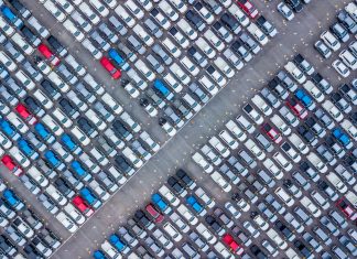 An aerial view of dozens of rows of new cars in a storage lot, ready for export