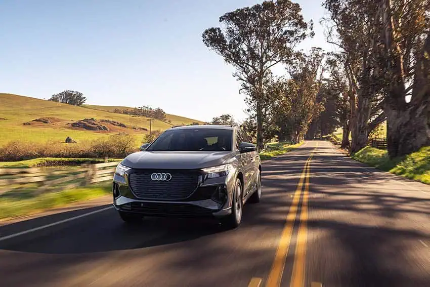An Audi Q4 electric car driving on an empty road surrounded by open land and trees
