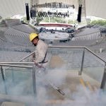 Man in uniform and hard hat spraying auditorium seats for mosquitos, surrounded by pesticide fumes.
