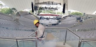 Man in uniform and hard hat spraying auditorium seats for mosquitos, surrounded by pesticide fumes.