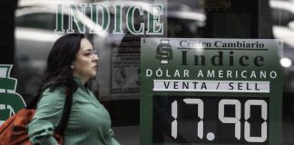 A woman walks by a sign stating the dollar-peso exchange rate to be 17.90.