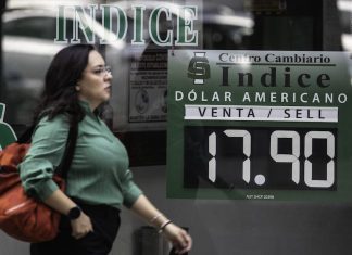 A woman walks by a sign stating the dollar-peso exchange rate to be 17.90.