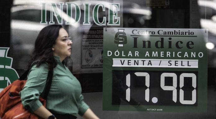 A woman walks by a sign stating the dollar-peso exchange rate to be 17.90.