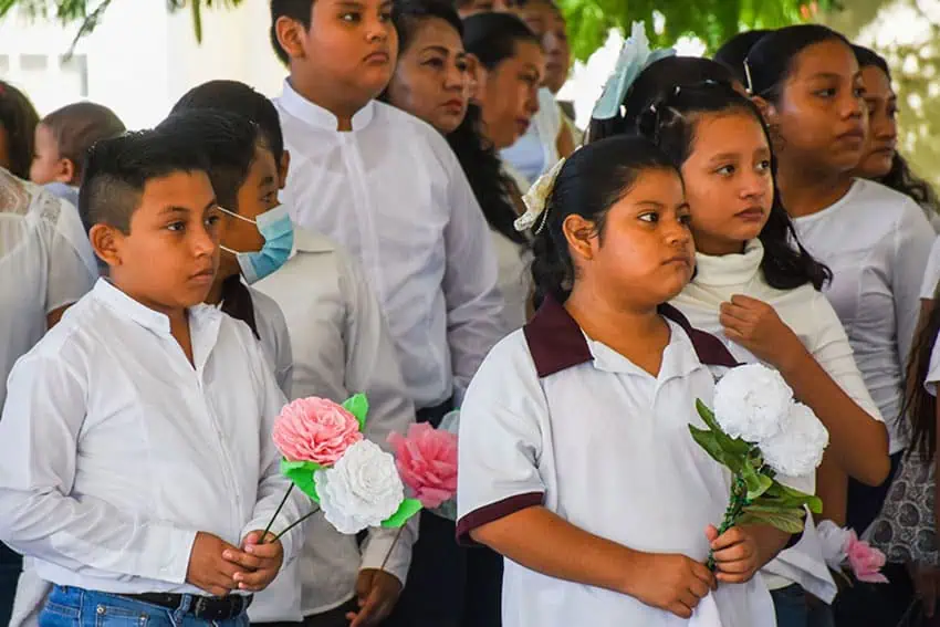 Somber looking primary school students holding chrysanthemums.