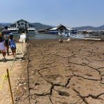 Family walking toward a marina in the Miguel Aleman reservoir in Mexico state. The lake bed they are walking on is cracked mud with no water.