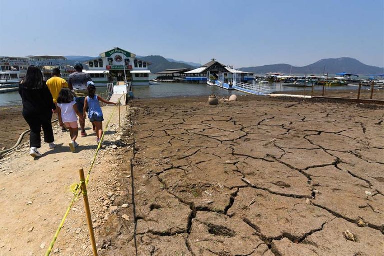 Family walking toward a marina in the Miguel Aleman reservoir in Mexico state. The lake bed they are walking on is cracked mud with no water.
