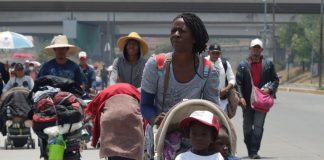 A group of mostly Black migrants, some of whom maybe be undocumented foreigners, walks down a Mexican highway under a bright sun.
