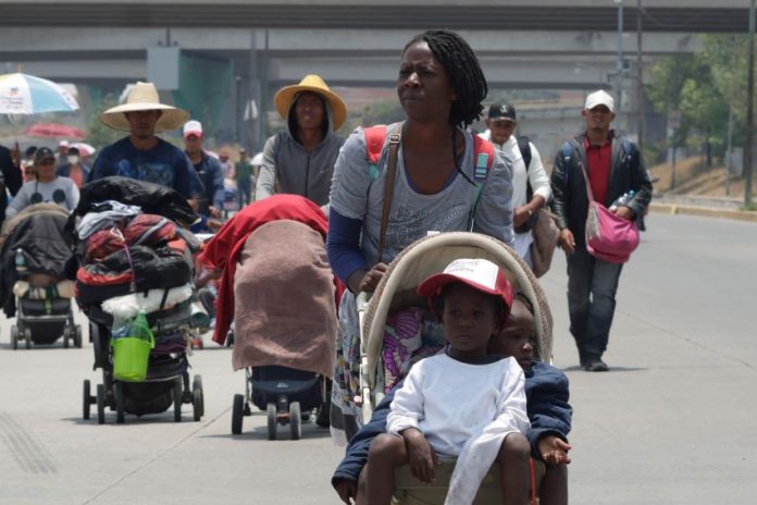 A group of mostly Black migrants, some of whom maybe be undocumented foreigners, walks down a Mexican highway under a bright sun.