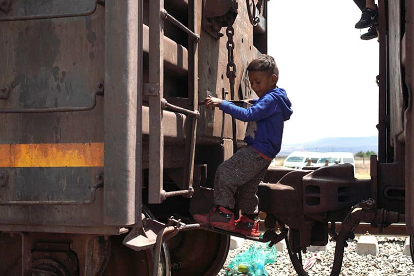 A boy about eight or nine years old from a migrant caravan in Mexico plays on the outside of a parked train car.