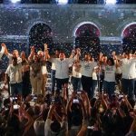 Morena gubernatorial candidate Javier May holds hands on stage with his campaign team, as confetti rains down.