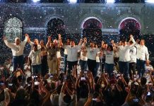 Morena gubernatorial candidate Javier May holds hands on stage with his campaign team, as confetti rains down.