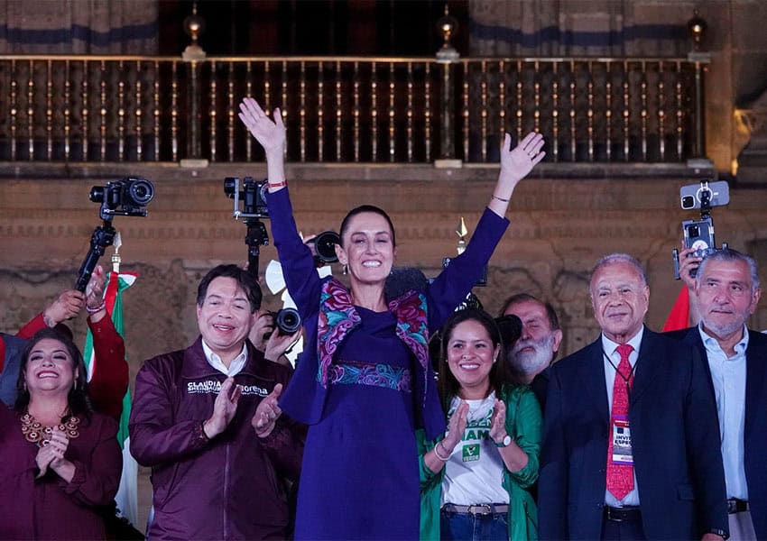 President-elect Claudia Sheinbaum standing with her arms in the air and in front a group of Morena party figures in Mexico City's zocalo main square, saluting crowds of her supporters.