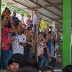 Refugees displaced by an armed attack on their Chiapas town stand in the bleachers of a open air sports court and look at proceedings below through a protective wire fence