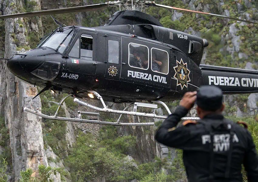 Man in a Mexican Fuerza Civil uniform watching the liftoff of a rescue helicopter with civilian passengers