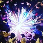 Members of the Jedi Knight Academy Mexico City at night gathered in a circle with each person extending their incandescent lightsabers to touch all together at the circle's center.