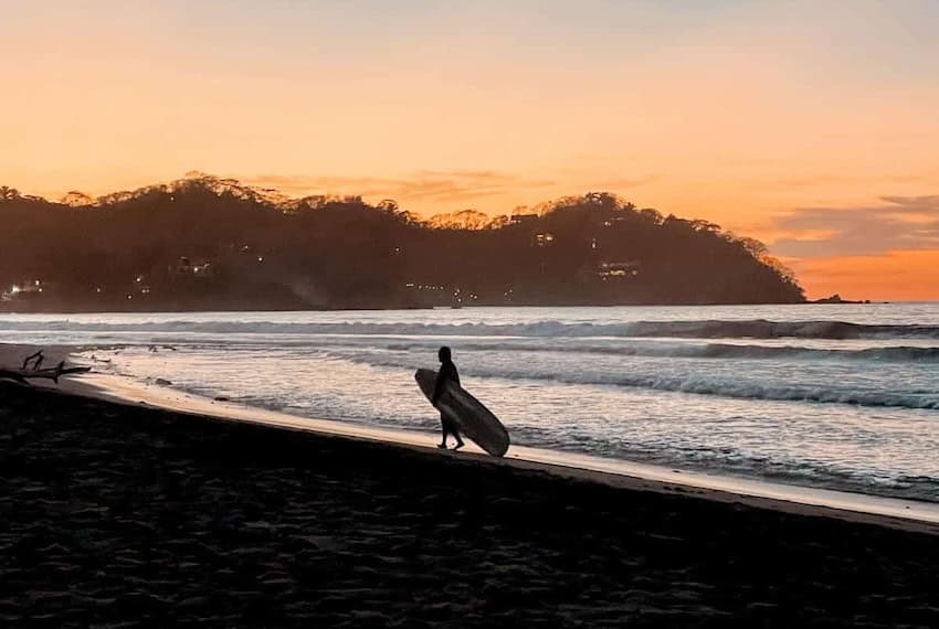 Surfer walking on the beach at sunset
