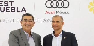 Puebla Governor Sergio Salomon and Audi Mexico President Tarek Mashour shaking hands in front of a temporary wall with the Audi logo.