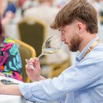 9 Mexican wines win Grand Gold Medals at Concours Mondial de Bruxelles Concours Mondial de Bruxelles wine taster seated in a large hall in Leon, Mexico, samples a white wine from a wine glass.