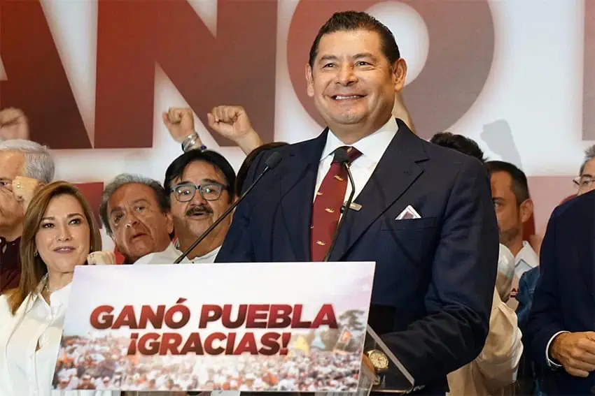 Alejandro Armenta, winner of Puebla's gubernatorial election according to early results, stands smiling at a podium with a sign reading "Ganó Puebla, ¡Gracias!"