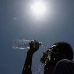 A person pours water on his face under blazing sun