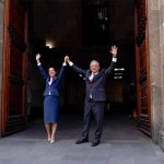 Claudia Sheinbaum and AMLO hold their hands in the air in the door of Mexico's National Palace.