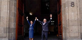 Claudia Sheinbaum and AMLO hold their hands in the air in the door of Mexico's National Palace.