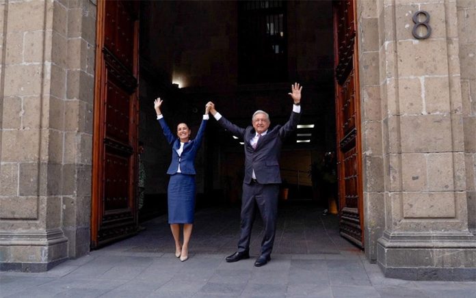 Claudia Sheinbaum and AMLO hold their hands in the air in the door of Mexico's National Palace.