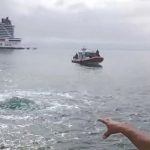 A fisherman points out the bubbling "water eye" in the ocean off Cozumel Island, with a cruise ship and another fishing boat in the background.