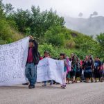 A long line of Mexican men women and children from Chiapas marching on a highway, holding makeshift cloth signs saying they were forced by violence to flee into Guatemala