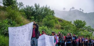 A long line of Mexican men women and children from Chiapas marching on a highway, holding makeshift cloth signs saying they were forced by violence to flee into Guatemala