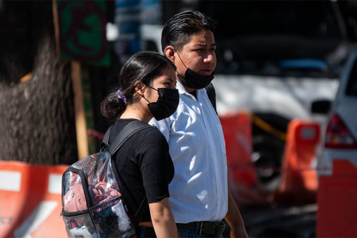 Two Mexico City residents side by side, a man and a woman, in the city wearing face masks to protect from COVID and other infections.