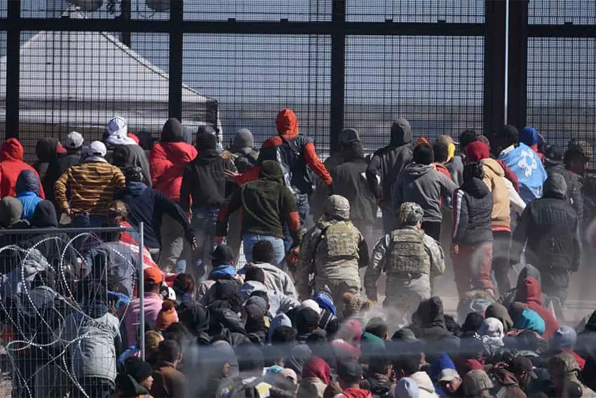 A crowd of migrants at the Ciudad Juarez/El Paso border staring at a tall mesh wire gate