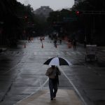 A person walks holding an umbrella in the rain