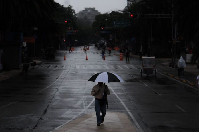 A person walks holding an umbrella in the rain