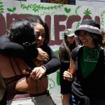 Pro-choice activists standing in front of a sign that says "Aborto Legal Puebla." Two activists are hugging while others look on smiling. as they celebrate the Puebla legislature's vote to decriminalize abortion.