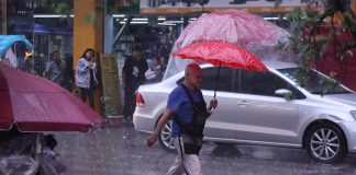 Man with red umbrella crosses street in the Mexico City historic center amid heavy rains.