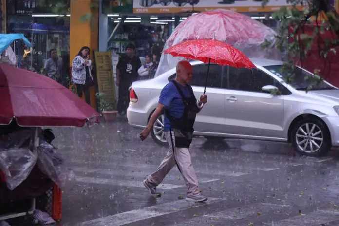 Man with red umbrella crosses street in the Mexico City historic center amid heavy rains.