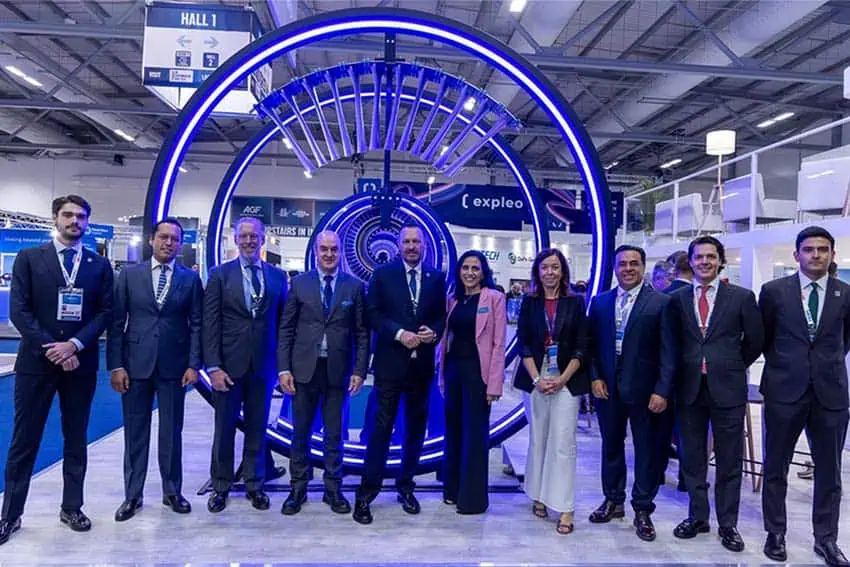 Officials with ITP Aero pose in a horizontal line with Queretaro Governor Mauricio Kuri in front of an artistic turbine display.