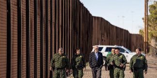 U.S. President Joe Biden walking with US Border Patrol officers along the U.S. border wall with a border patrol SUV parked in the background.